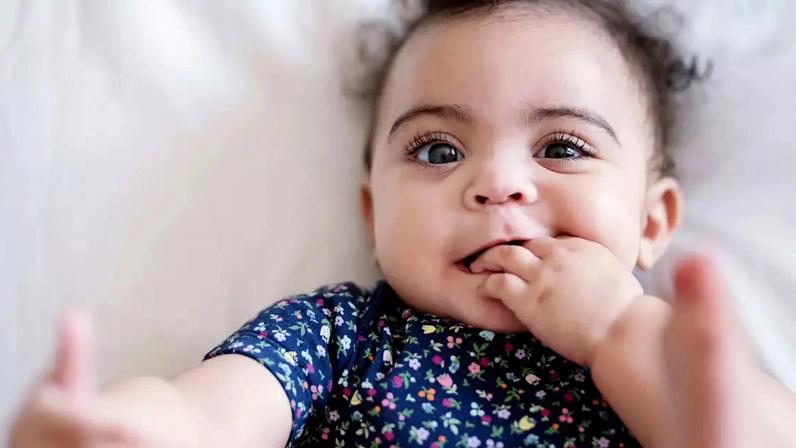 Bebê com uma mão da boca e outra no pé