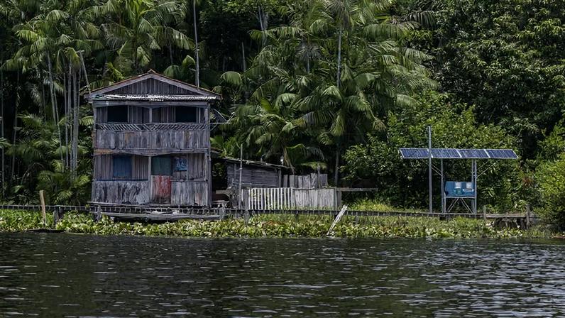 Casa de madeira à beira do rio: residência típica da Amazônia às margens de um rio no arquipélago de Marajó, com painéis fotovoltaicos para captação de energia solar.