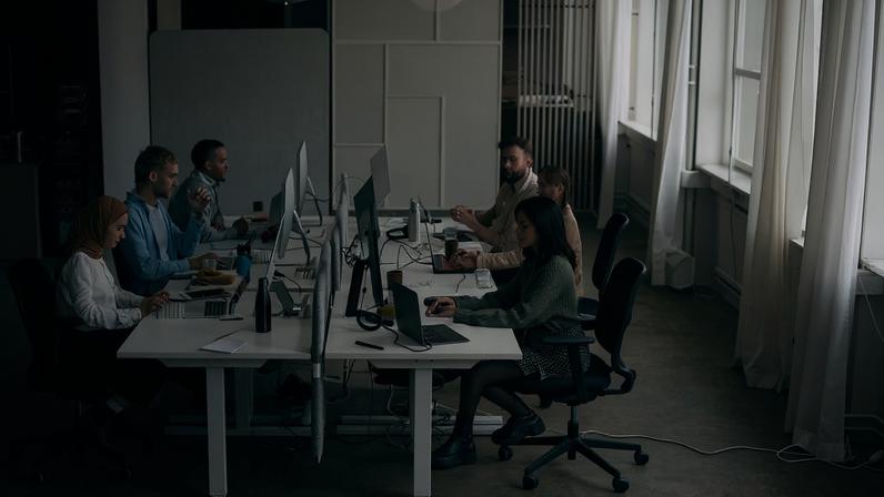 High angle view of busy programmers working on computers and laptops while sitting around desk at office.