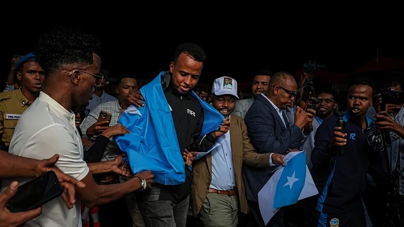 O árbitro somali Omar Abdulkadir Artan, envolto na bandeira da Somália, é cercado por apoiadores após sua chegada a Mogadíscio, na Somália, em 9 de junho de 2026.