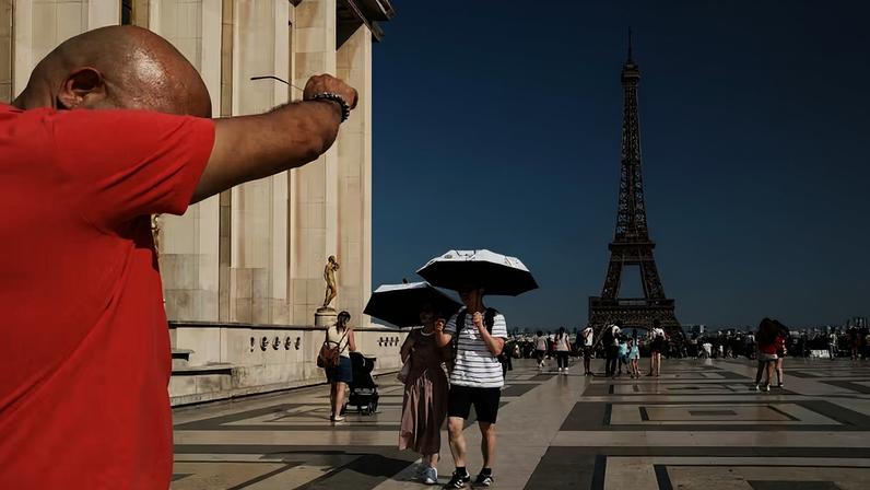 Homem sua sob calor intenso enquanto turistas usam guarda-chuva para se proteger do sol na região do Trocadéro, em frente à Torre Eiffel, durante onda de calor na França, em junho de 2026.