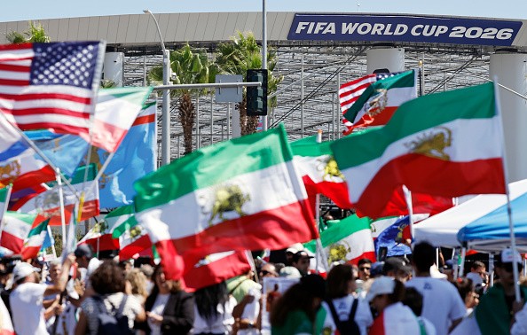 Manifestantes protestam contra a República Islâmica do Irã, exibindo bandeiras iranianas pré-revolucionárias e outras bandeiras, em frente ao Estádio de Los Angeles, antes da partida da seleção iraniana de futebol contra a Nova Zelândia pela Copa do Mundo, em 15 de junho de 2026.