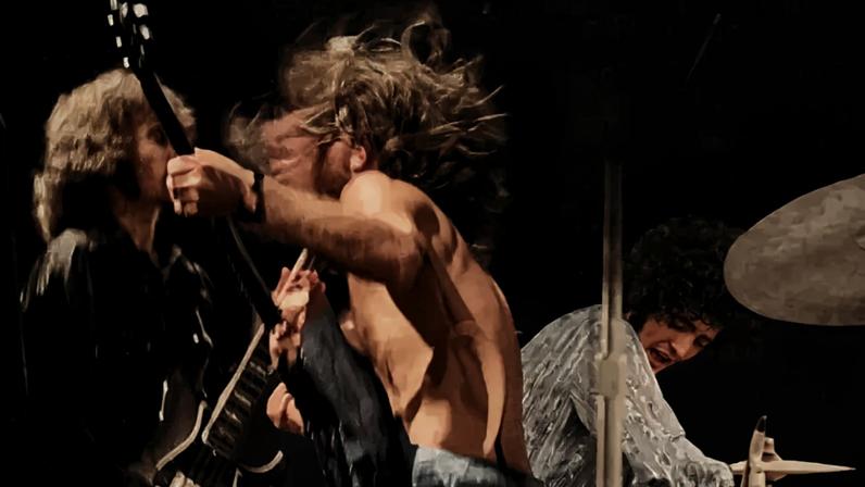 Três músicos em preto e branco, com cabelo comprido, tocando instrumentos. Um guitarrista à esquerda, outro no centro com cabelo em movimento, e um baterista à direita com expressão intensa