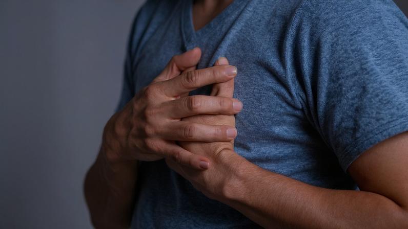 Foto colorida de um homem com blusa azul e mãos no peito, com sintomas de infarto - Metrópoles.