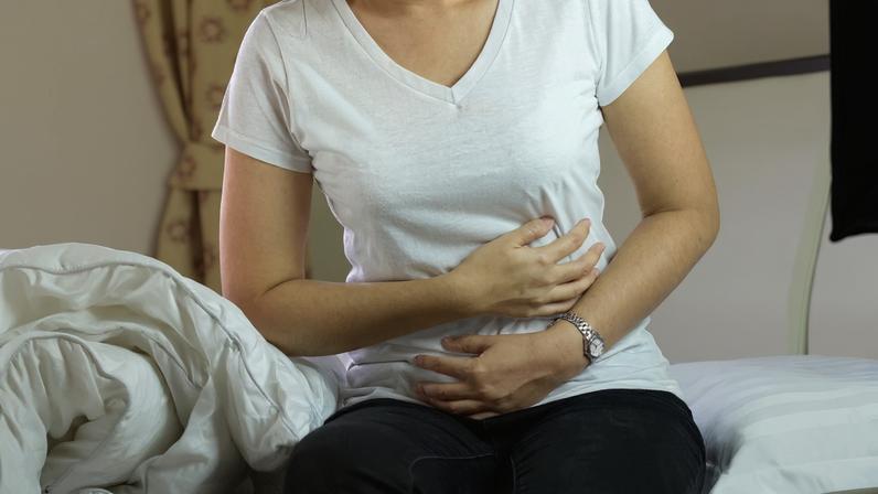 Mulher leva as mãos ao intestino como sinal de dor - e esse é um dos sintomas da Síndrome do Intestino Irritável