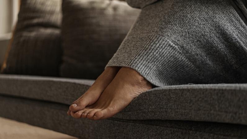 Foto em close-up dos pés de uma mulher sentada no sofá - Angiologista explica por que mãos e pés gelados podem indicar doenças - Metrópoles
