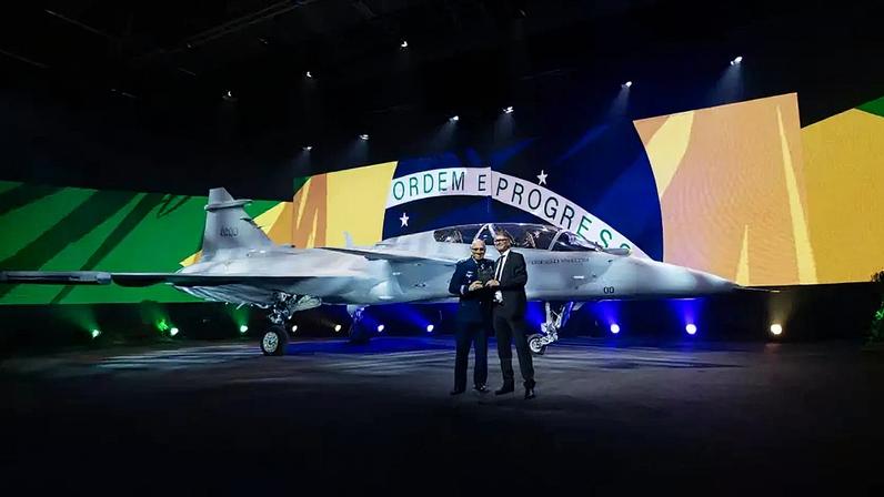 O ministro da Defesa, José Mucio, com o CEO da Saab, Micael Johansson, com o caça Gripen F ao fundo (Foto: Divulgação-Saab)