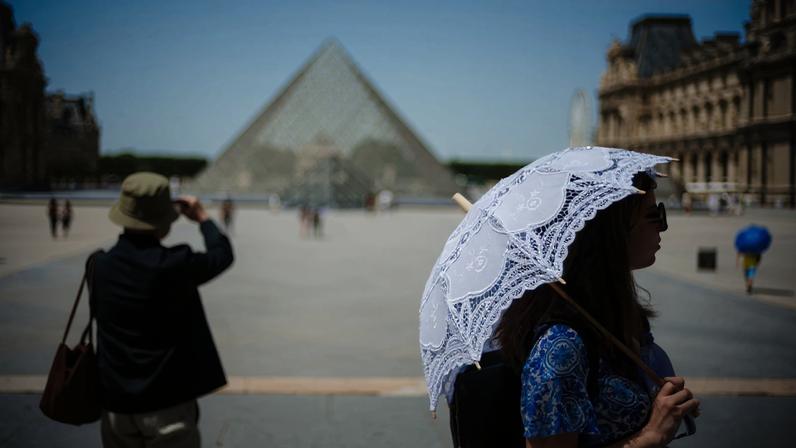 Uma turista se protege do sol sob um guarda-sol em frente à Pirâmide do Louvre