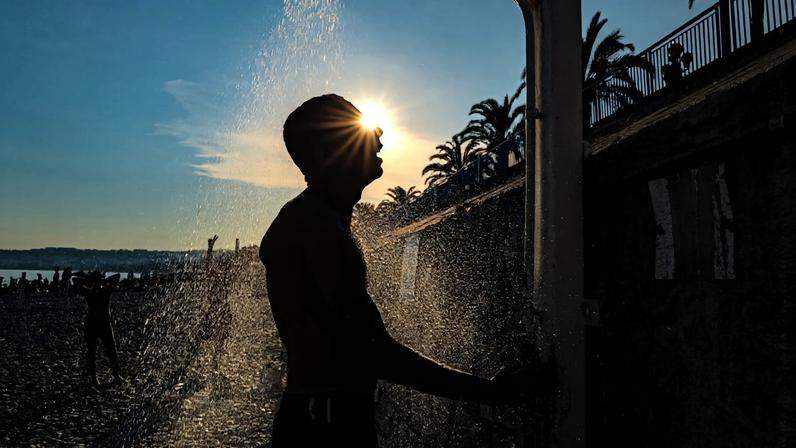 Um homem toma banho de chuveiro na praia, ao longo da "Promenade des Anglais", na cidade de Nice, na Riviera Francesa