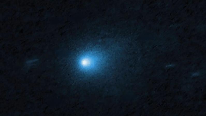 Cometa azul brilhante com cauda difusa, cercado por múltiplos traços de estrelas brancas em um fundo escuro do espaço