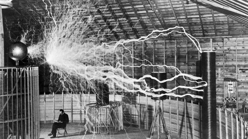 Montagem fotográfica usando dupla exposição mostra Nikola Tesla sentado na sala onde está instalado seu gerador de alta voltagem, em 1899. (Foto: Dickinson Alley/Wikimedia Commons/Domínio público)