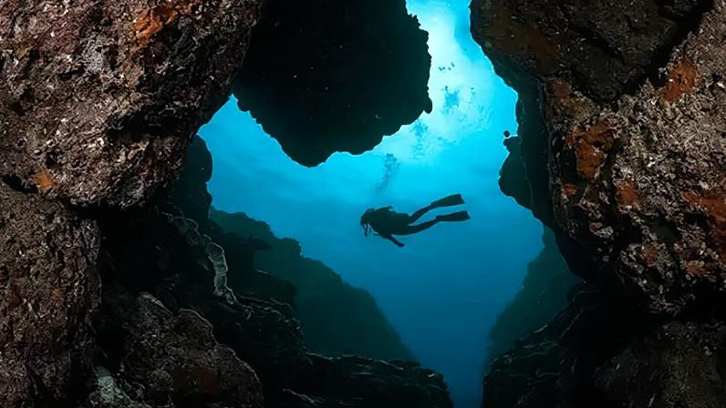 Jay Clue A scuba diver swims through a narrow canyon framed by rugged rock walls (Credit: Jay Clue)