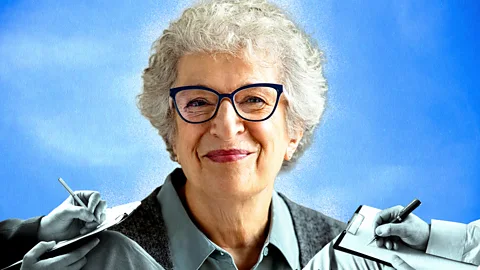 An older woman with white hair and glasses smiles, while the hands of therapists writing notes surround her (Credit: Serenity Strull/ BBC/ Getty Images)