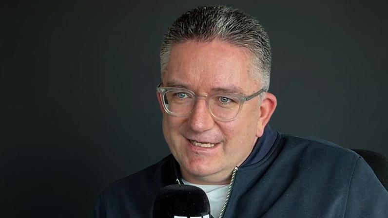 A man, Dan Finley, with grey hair and clear glasses, holding a mic.