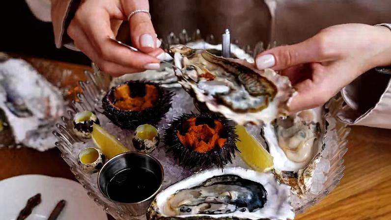 Uma pessoa se serve em um prato de frutos do mar com ostras e ouriço