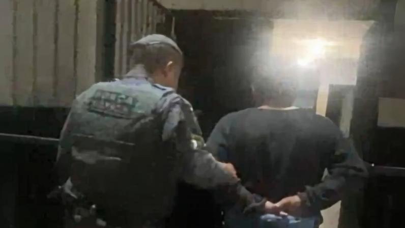 Foto colorida do momento em que homem foragido por homicídio é conduzido pela Polícia Militar.