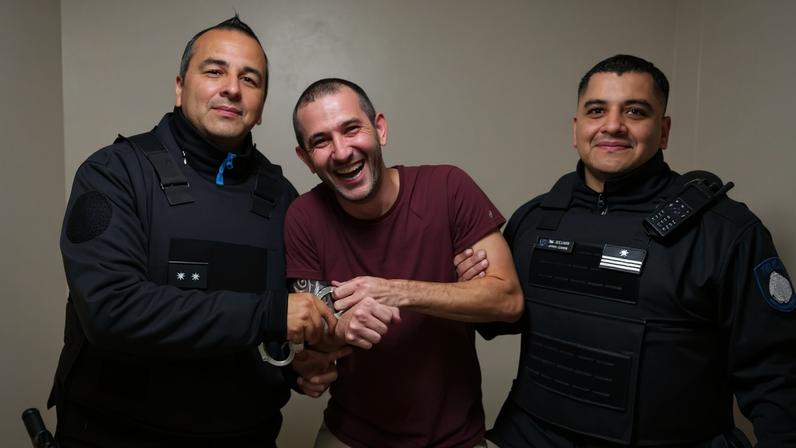 Wellington Firmino, condenado pelos ataques aos Três Poderes, posa para foto com algemas ao lado de policiais da Argentina que verificam porque ele descumpriu ordem de prisão domiciliar e trocou de casa.