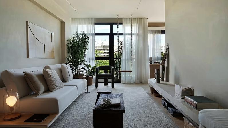 LIVING | O sofá Linares, da LZ Studio, harmoniza bem com as paredes na cor Algodão Egípcio, da Suvinil. À frente, o baú Caixote Antigo, da Casa Ocre, confere efeito rústico, enquanto o tapete Marut Fendi White, da Galeria Hathi, suaviza o espaço. A poltrona Nala, em buclê verde, o balanço de madeira maciça e macramê, e o quadro decorativo Livadi, também são da Casa Ocre. O paisagismo é da Horto Girassol