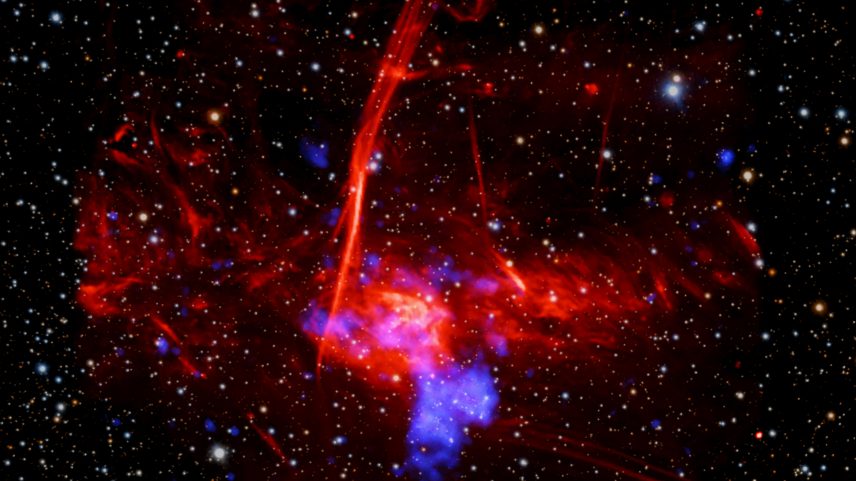 Set against a backdrop packed with distant stars and other specks of light are two distinct, overlapping clouds. The larger, visually dominant cloud, is red and multifaceted. It has an irregular shape, and features patches of different textures, including pockets that resemble wispy smoke, tangles of faint red veins, and clear streaking lines. This large cloud of expanding gas represents radio data from the MeerKAT telescope in South Africa. Overlapping with that red cloud is a cloudy blue blob representing X-ray data from NASA's Chandra X-ray Observatory and ESA's XMM-Newton.
