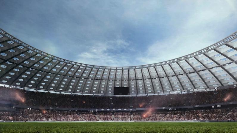 Vista de campo de futebol em estádio cheio de torcedores, com cobertura curva e céu claro. Sinalizadores acendendo.