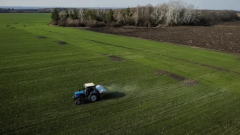 Vista aérea mostra um trator espalhando fertilizante em um campo de trigo perto de Yakovlivka