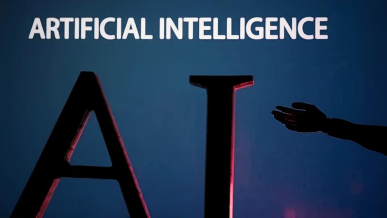 Foto ilustrativa mostra as letras “AI” (Inteligência Artificial) e uma miniatura de mão robótica