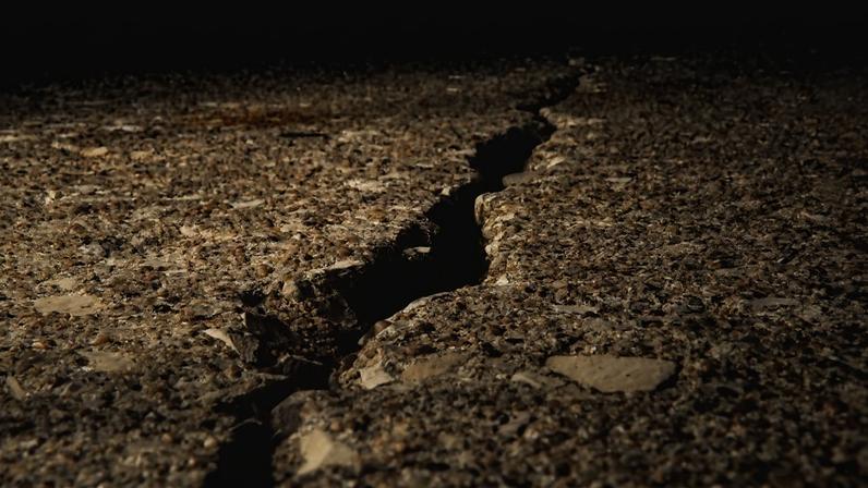 Um solo rachado coberto de pedras sob a luz do sol, com um fundo desfocado. Metrópoles
