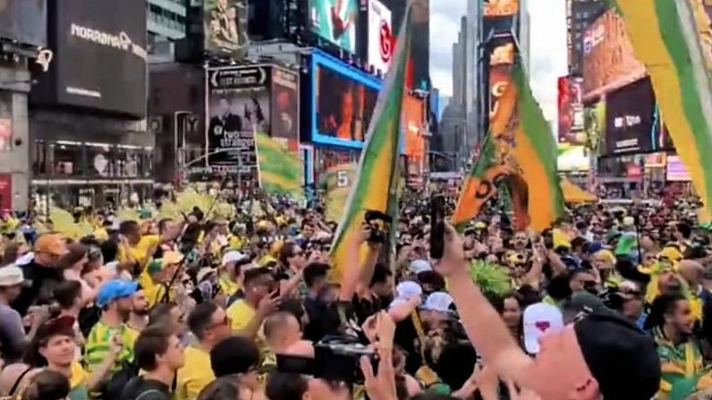 Na imagem, torcedores brasileiros reunidos na Times Square com camisas da seleção e bandeiras