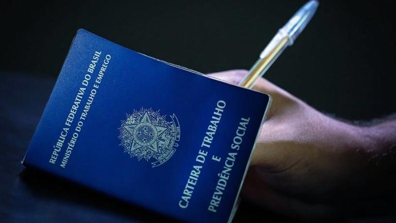 Abimaq estima alta de 12,7% nos custos de mão de obra com PEC do fim da escala 6 X 1; na imagem, mão segurando uma caneta e preenchendo uma carteira de trabalho