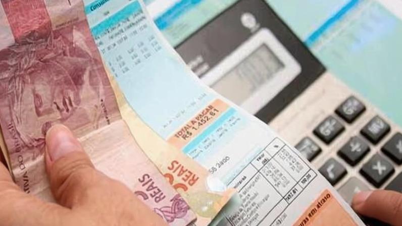Uma mulher segura uma conta de luz enquanto digita em uma calculadora