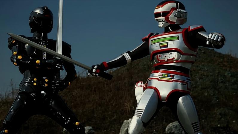 Dois personagens de tokusatsu, um de armadura preta brilhante com detalhes amarelos e outro prateada com detalhes vermelhos e coloridos, duelam com espadas em um cenário árido