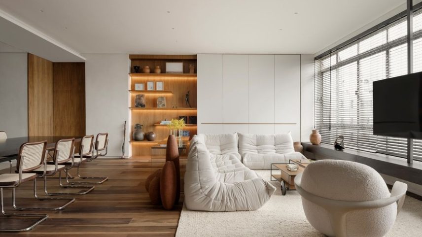 LIVING | Agora integrado, o espaço reúne salas de estar e jantar, tendo o piso de tábuas corridas de canela imperial de demolição, da Parket, como elemento de unidade visual. O tapete de chenille existente demarca a área de estar, onde se destaca o sofá modular da linha Togo, de Michel Ducaroy para Ligne Roset, herança de família. Logo atrás, o conjunto de vasos Terra, de Domingos Tótora, acompanha o aparador de vidro desenhado pela arquiteta e produzido pela Vidraçaria GRTM. Também assinados pela arquiteta, a estante com prateleiras iluminadas e o armário com portas mimetizadas foram executados em folha de freijó natural e MDF com microtextura off-white pela Marcenaria Londrina. No móvel, sobressaem a peça azul de Marco Tulio Resende, a caixa de Thais Helt e esculturas de Amilcar de Castro