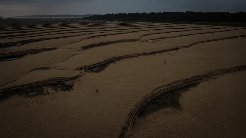 Ribeirinhos atravessam o leito seco de um braço do rio Solimões, no município de Tefé, durante seca extrema de 2024