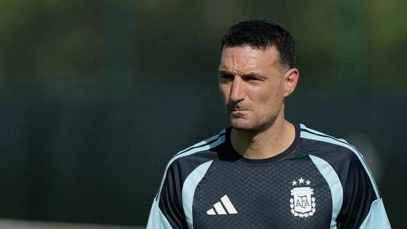 Homem de cabelo curto e escuro veste camiseta preta com detalhes em azul claro e escudo da Associação de Futebol Argentino (AFA). Fundo desfocado em verde.