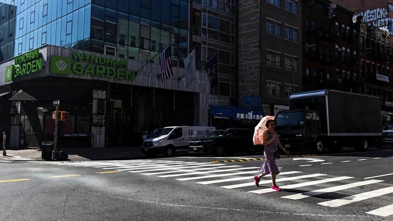 Pedestre se protege do sol com um guarda-chuva ao atravessar uma rua em Manhattan, Nova York, durante onda de calor