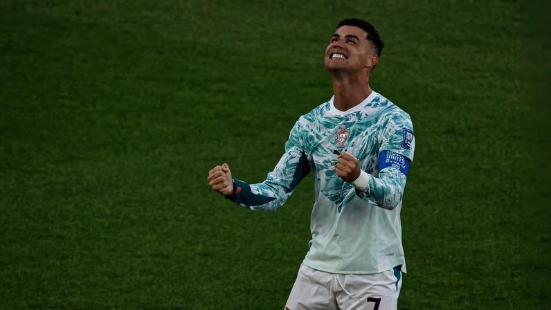 Jogador com uniforme branco e verde do time de Portugal levanta os punhos e olha para cima em comemoração no gramado.