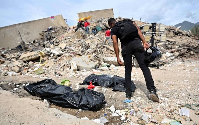 Homem observa sacos mortuários em escombros de edifícios em Caraballeda, no estado de La Guaira, na Venezuela
