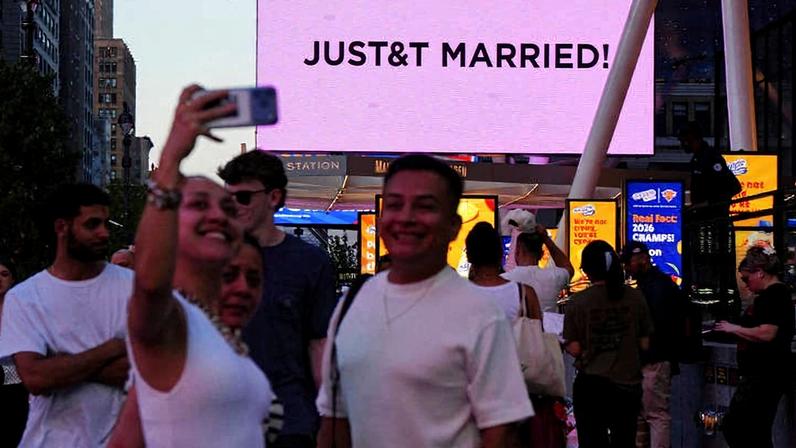 Pessoas tiram selfies ao lado de telão que exibe mensagem sobre casamento de Taylor Swift e Travis Kelce