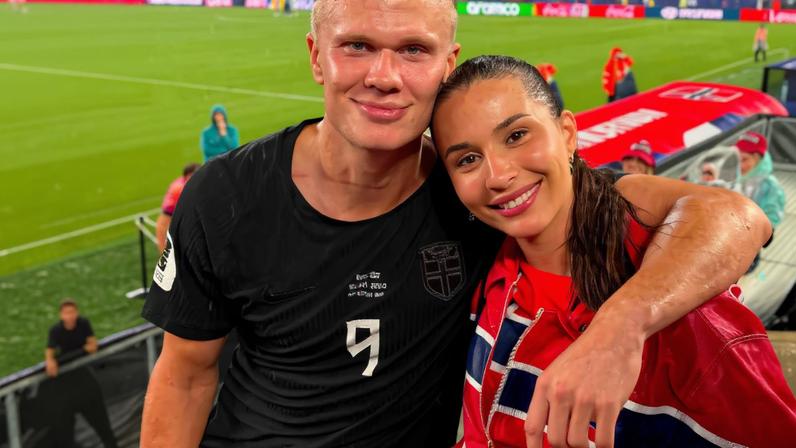 À esquerda, mulher com cabelo longo e franja tira selfie em espelho segurando celular preto. À direita, homem com uniforme preto de futebol e mulher com jaqueta vermelha com detalhes em azul e branco posam abraçados em estádio.