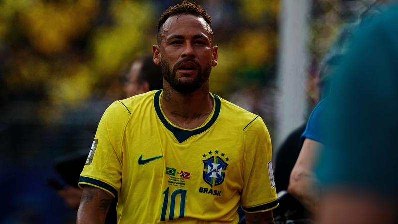 Neymar veste a camisa amarela da seleção brasileira com o número 10 durante partida. Fundo desfocado mostra torcida com camisas amarelas.