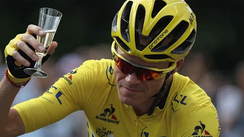 Chris Froome, wearing the overall leader's yellow jersey, is handed a glass of champagne as he rides to victory on the final stage of the 2016 Tour de France.