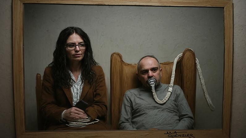 Julia Quenzler Salem Michel Al-Salem in a court sketch - he is on the right of the picture with a breathing tube on his mouth, a grey sweatshirt, he has a bald head and is slumped in an armchair. The tube makes his expression unclear. His translator, a woman with black shoulder length hair, a brown blazer, white shirt, and glasses, is sitting next to him