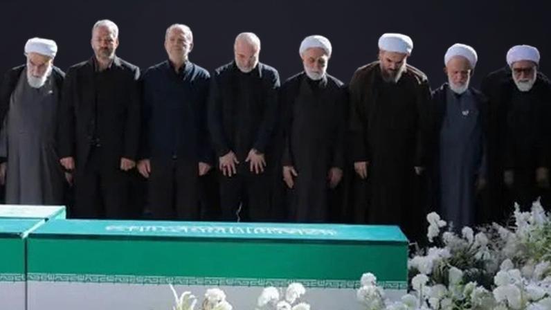 Reuters Iranian President Masoud Pezeshkian, Iran's Parliament speaker Mohammad Baqer Qalibaf and Chief Justice of Iran Gholam-hossein Mohseni Ejei with officials attend a prayer during a public farewell ceremony to pay their respects to late Supreme Leader Ayatollah Ali Khamenei. A large crowd can be seen in the background as everyone stands looking at the coffin