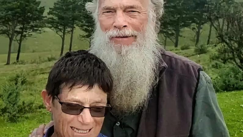 Nick Bailey Rodney Saunders stands behind Rachel. Rodney has a long grey beard while Rachel has dark hair and is wearing sunglasses