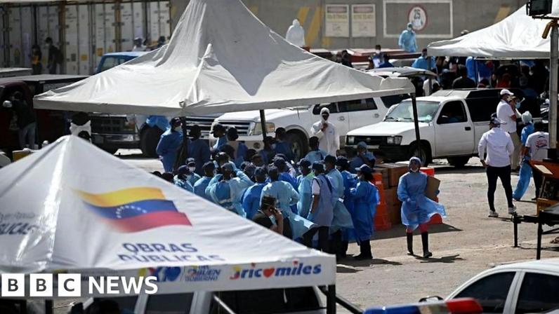 A group of staff officers in blue protective wear stand beneath a white tent