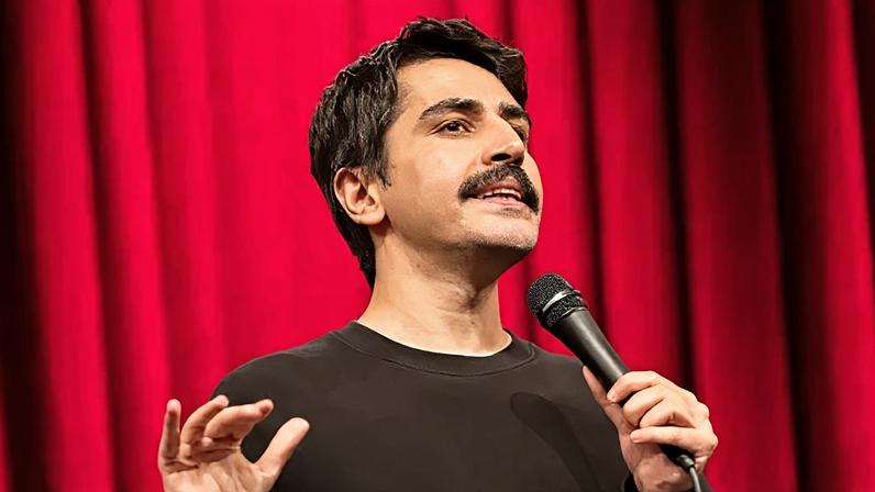Instagram/@denizgoktasx A head-shot posted by a Turkish stand-up comic showing him holding a microphone and standing in front of a red curtain