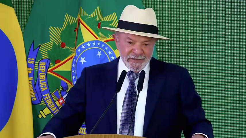 Presidente Luiz Inácio Lula da Silva, de chapéu bege e terno azul-marinho, discursa em um púlpito de madeira diante de bandeira e brasão do Brasil ao fundo.