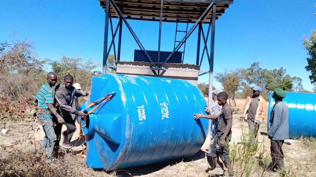 Pessoas levando uma caixa d'água azul para a estrutura do poço inaugurado em Bata-Bata, em Angola