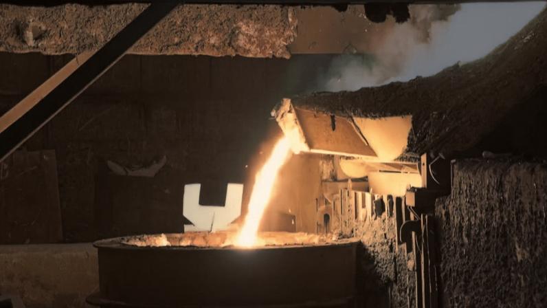 Metal líquido incandescente sendo despejado em recipiente durante processo industrial de fundição de aço
