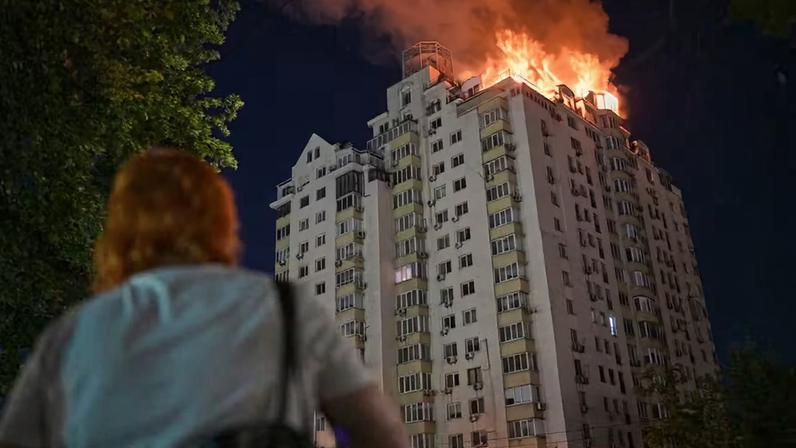 Uma mulher observa um prédio de apartamentos em chamas após um ataque de míssil russo em Kiev, Ucrânia, na quinta-feira, 2 de julho de 2026 — Foto: AP/Danylo Antoniuk